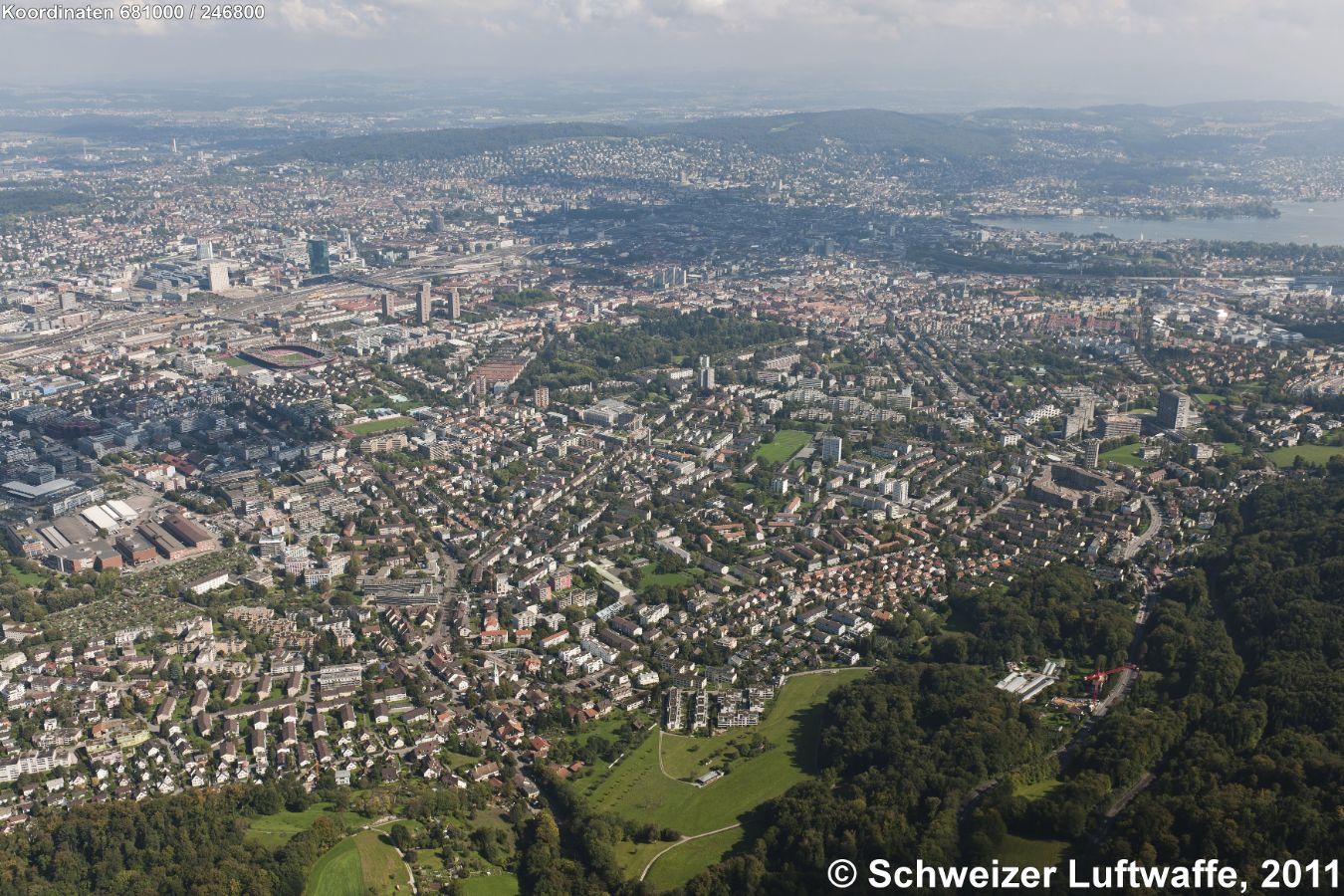 Im Vordergrund: links: ZH - Altstetten, rechts: ZH - Albisrieden; Siedlung in der Waldlichtung unten Mitte: 'Brünneliacker'. Bildmitte links: Stadion Letzigrund. Waldfläche Bildmitte: Friedhof Sihlfeld. Gegen linke obere Bildecke: Zürich-Oerlikon. Zürich-See oben rechs, im Schatten der Aufnahme Rchtg. Nord: Universität und ETH.